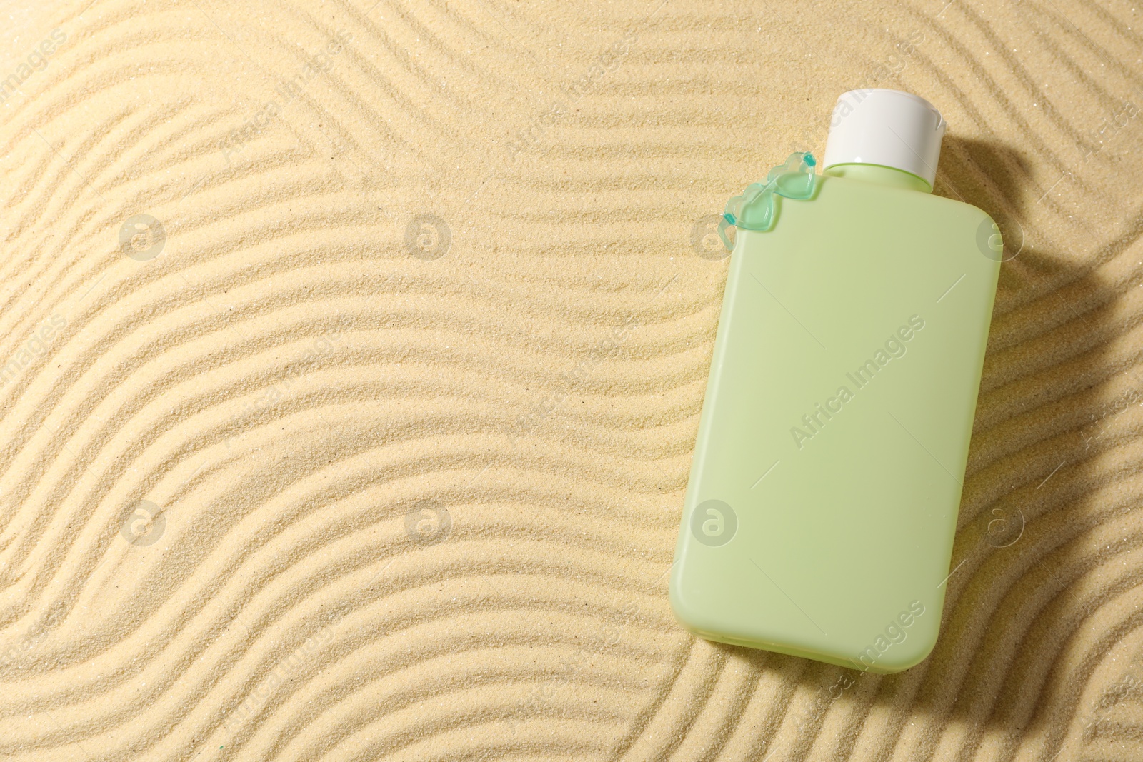 Photo of Bottle of sun protection product on sand, top view. Space for text