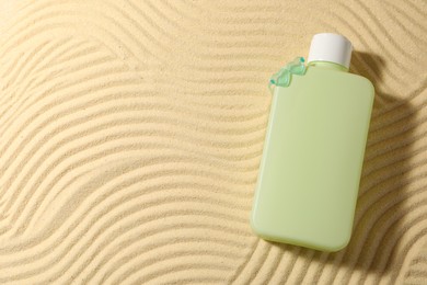 Bottle of sun protection product on sand, top view. Space for text