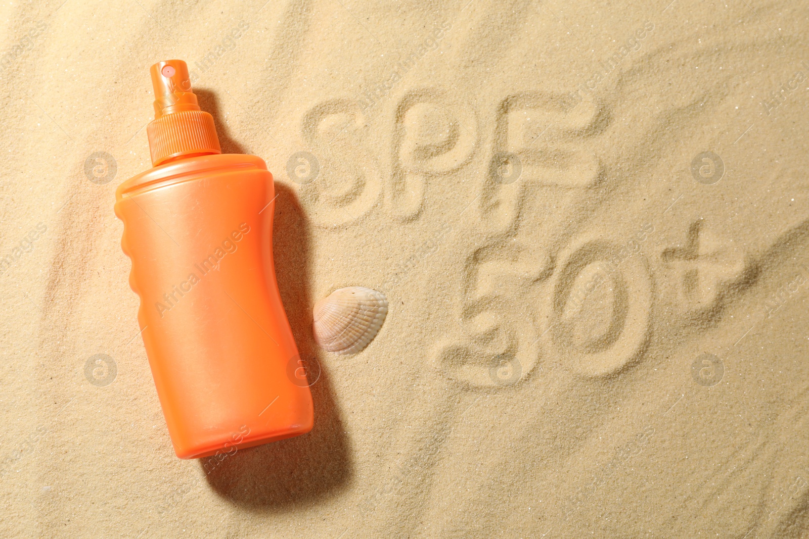 Photo of Abbreviation SPF 50 written on sand, bottle of sun protection product and seashell at beach, top view