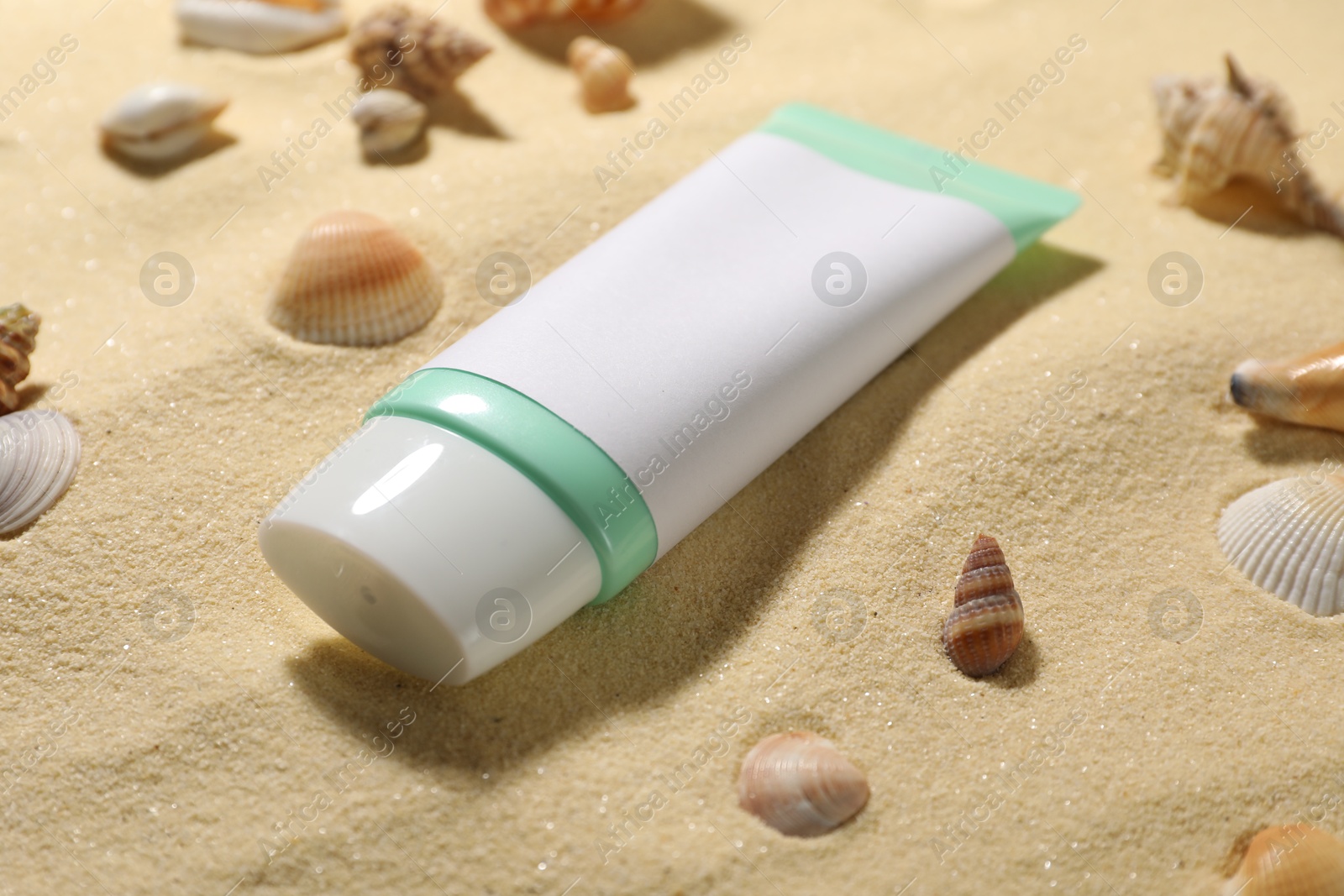 Photo of Tube of sun protection product and seashells on sand, closeup