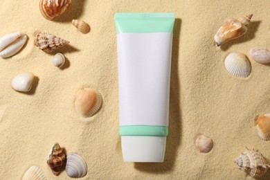 Photo of Tube of sun protection product and seashells on sand, flat lay