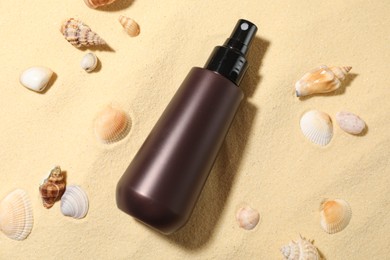 Photo of Bottle of sun protection product and seashells on sand, flat lay