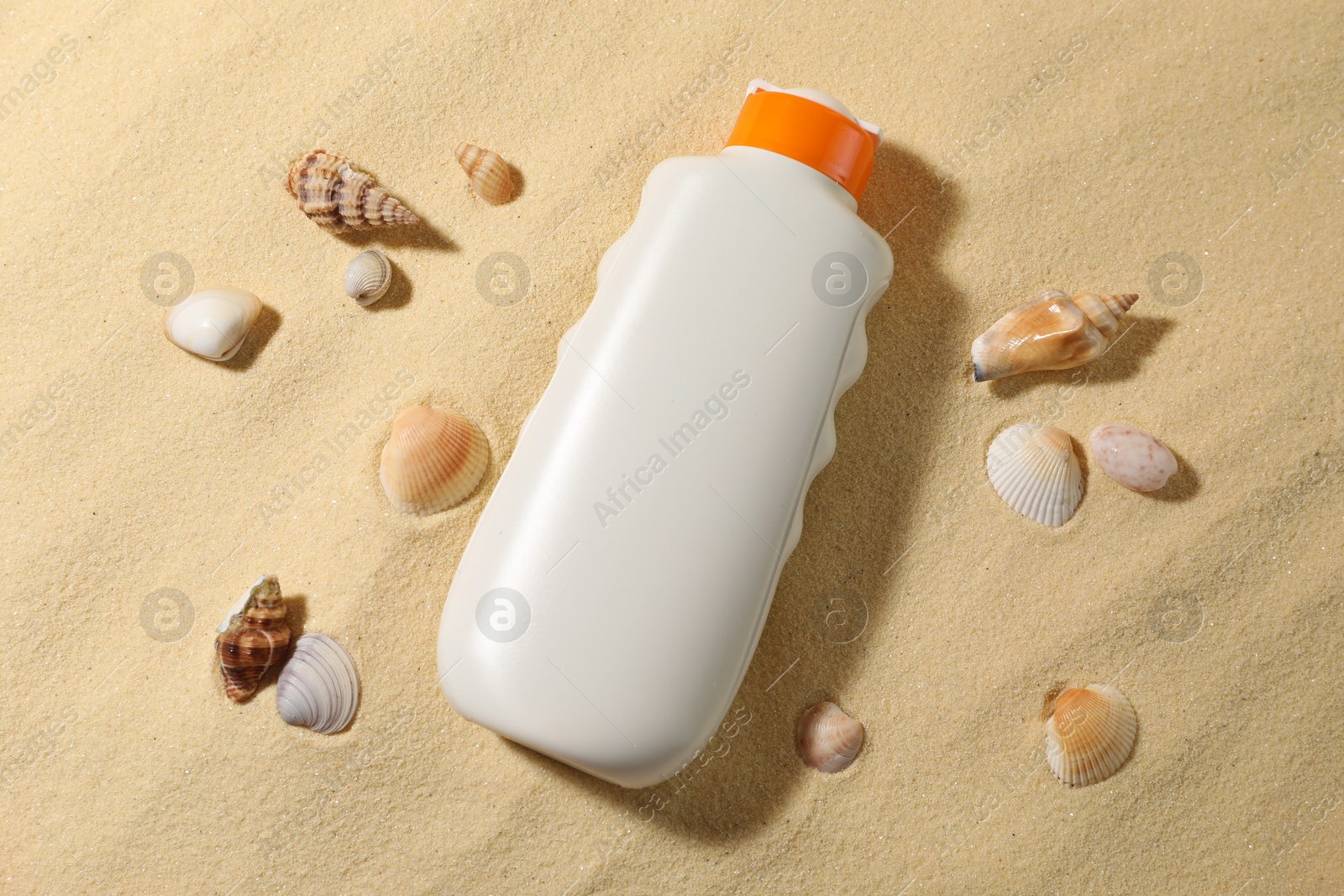 Photo of Bottle of sun protection product and seashells on sand, flat lay