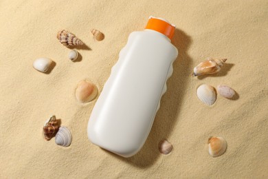 Bottle of sun protection product and seashells on sand, flat lay