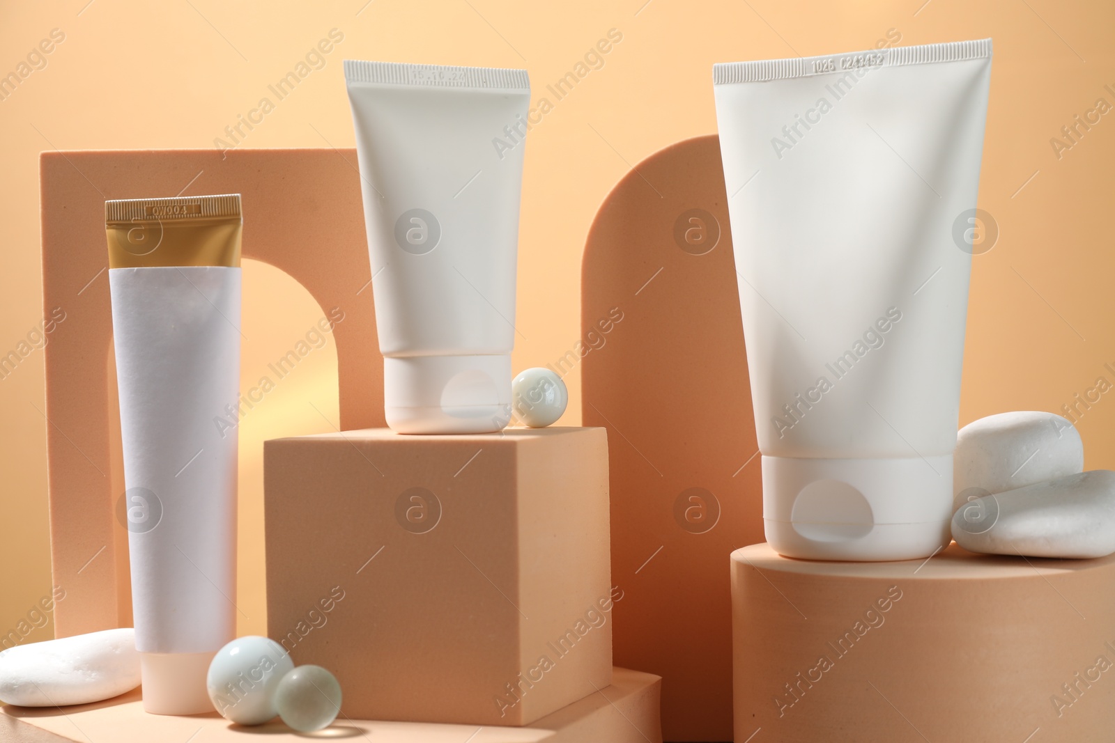 Photo of Tubes of sun protection product, decorative stones and podiums on beige background