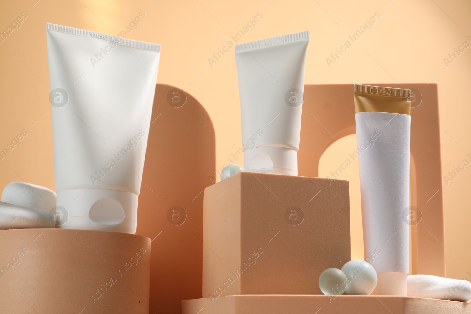 Photo of Tubes of sun protection product, decorative stones and podiums on beige background, low angle view