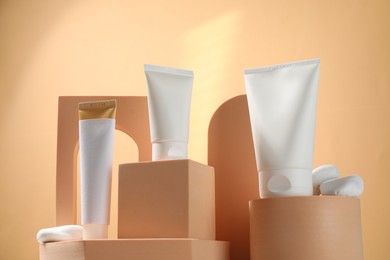 Tubes of sun protection product, decorative stones and podiums on beige background, low angle view