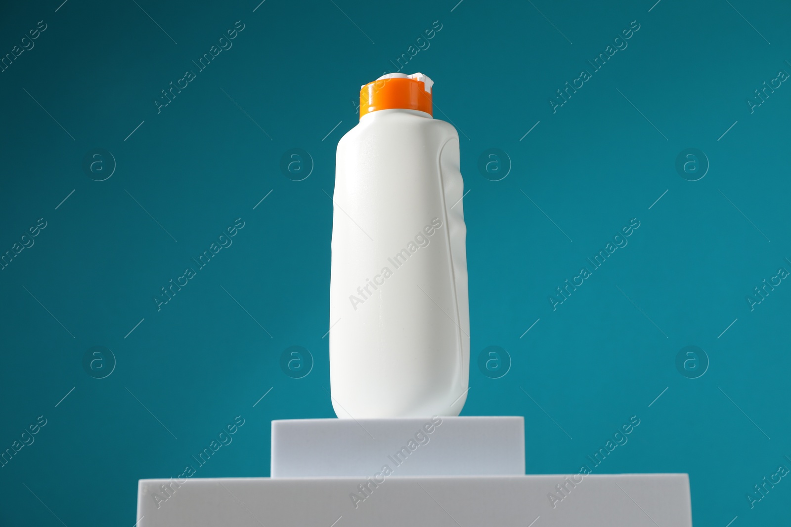 Photo of Bottle of sun protection product on podium against light blue background, low angle view