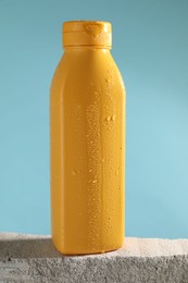 Photo of Bottle of sun protection product on stone against light blue background