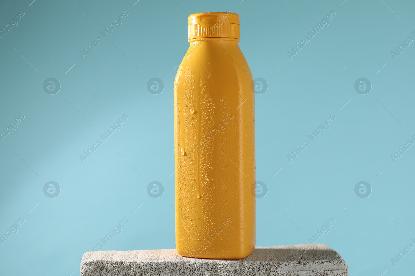 Photo of Bottle of sun protection product on stone against light blue background