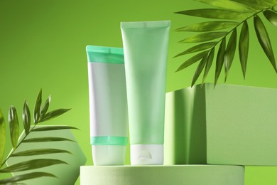 Tubes of sun protection product, branches and podiums against green background