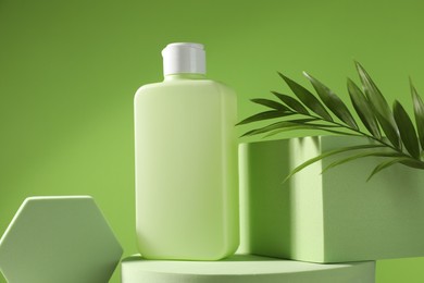 Photo of Bottle of sun protection product, branch and podiums against green background