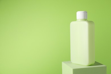 Bottle of sun protection product on podium against green background, space for text