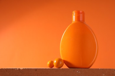 Bottle of sun protection product and decor on stone against orange background, space for text