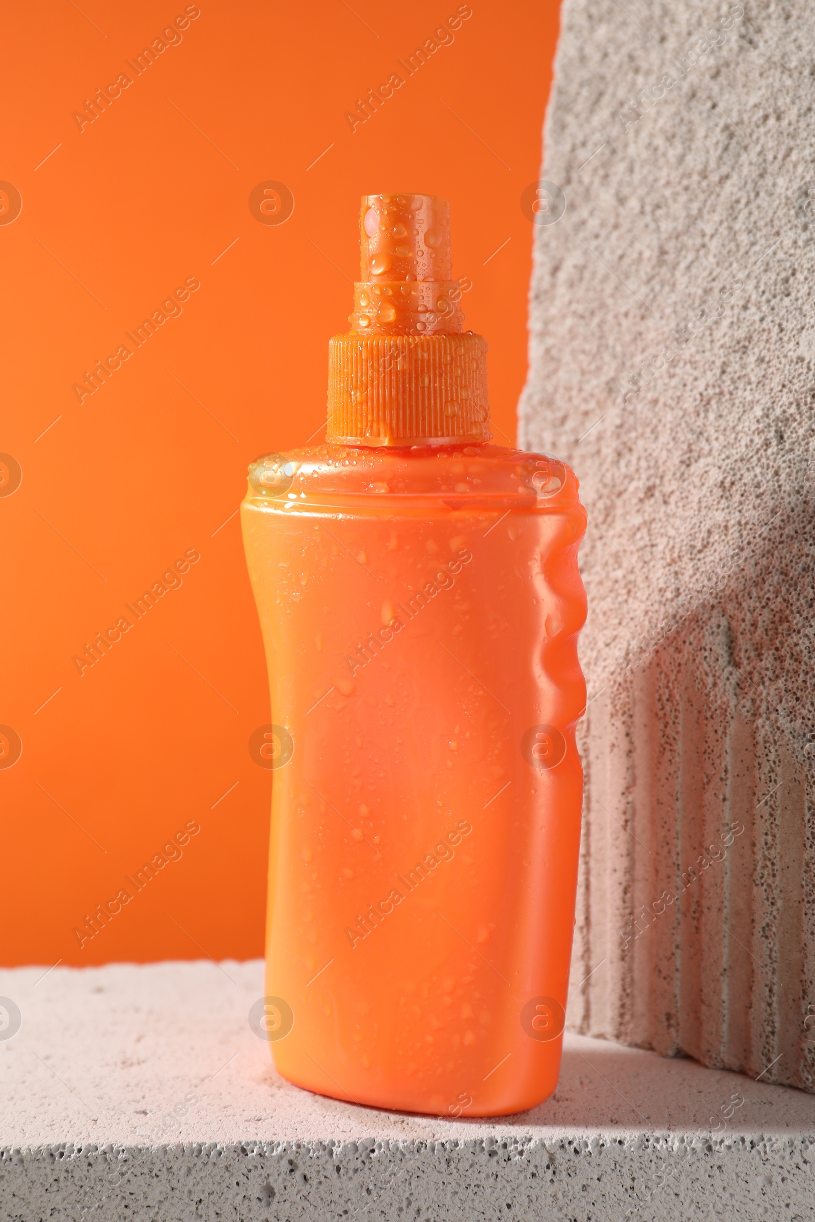 Photo of Bottle of sun protection product on stone against orange background