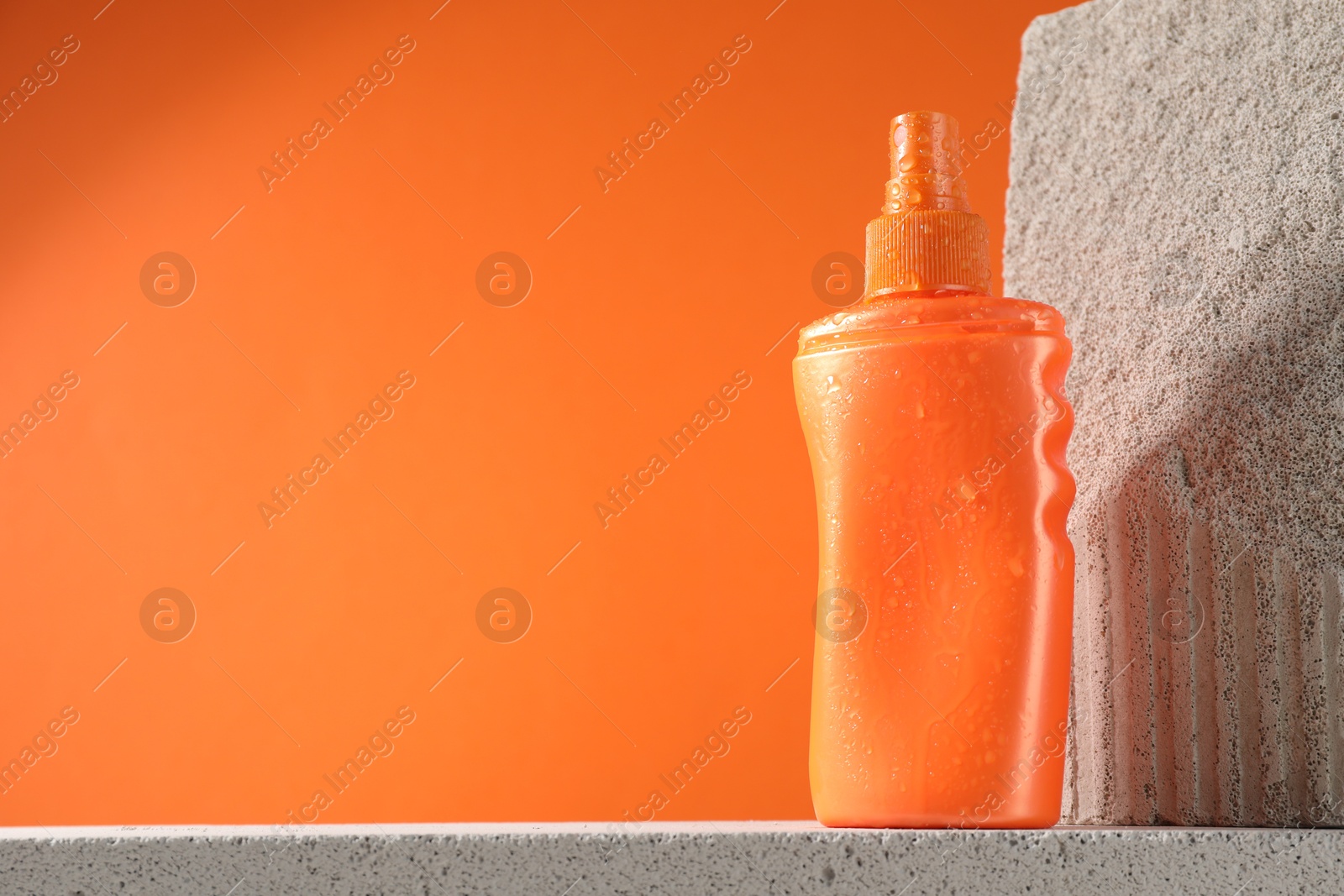 Photo of Bottle of sun protection product on stone against orange background, space for text