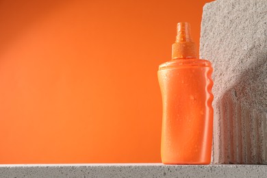 Bottle of sun protection product on stone against orange background, space for text