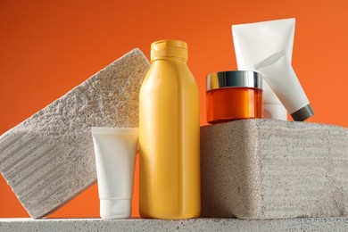 Different sun protection products and stones on orange background