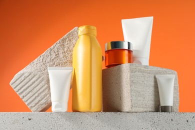 Different sun protection products and stones on orange background