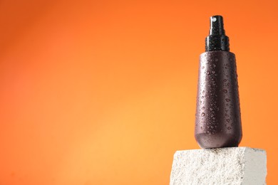 Photo of Bottle of sun protection product on stone against orange background, space for text