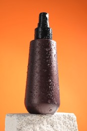 Photo of Bottle of sun protection product on stone against orange background