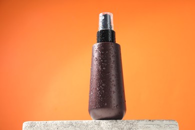 Bottle of sun protection product on stone against orange background