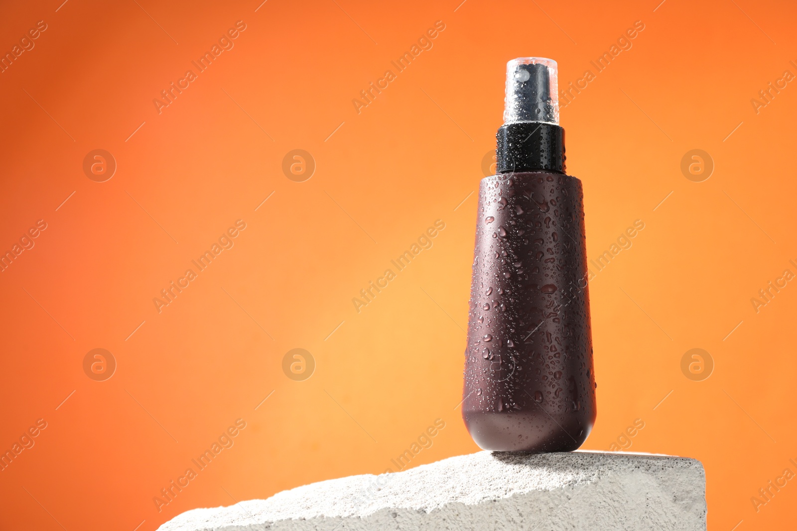 Photo of Bottle of sun protection product on stone against orange background, space for text