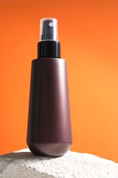 Bottle of sun protection product on stone against orange background