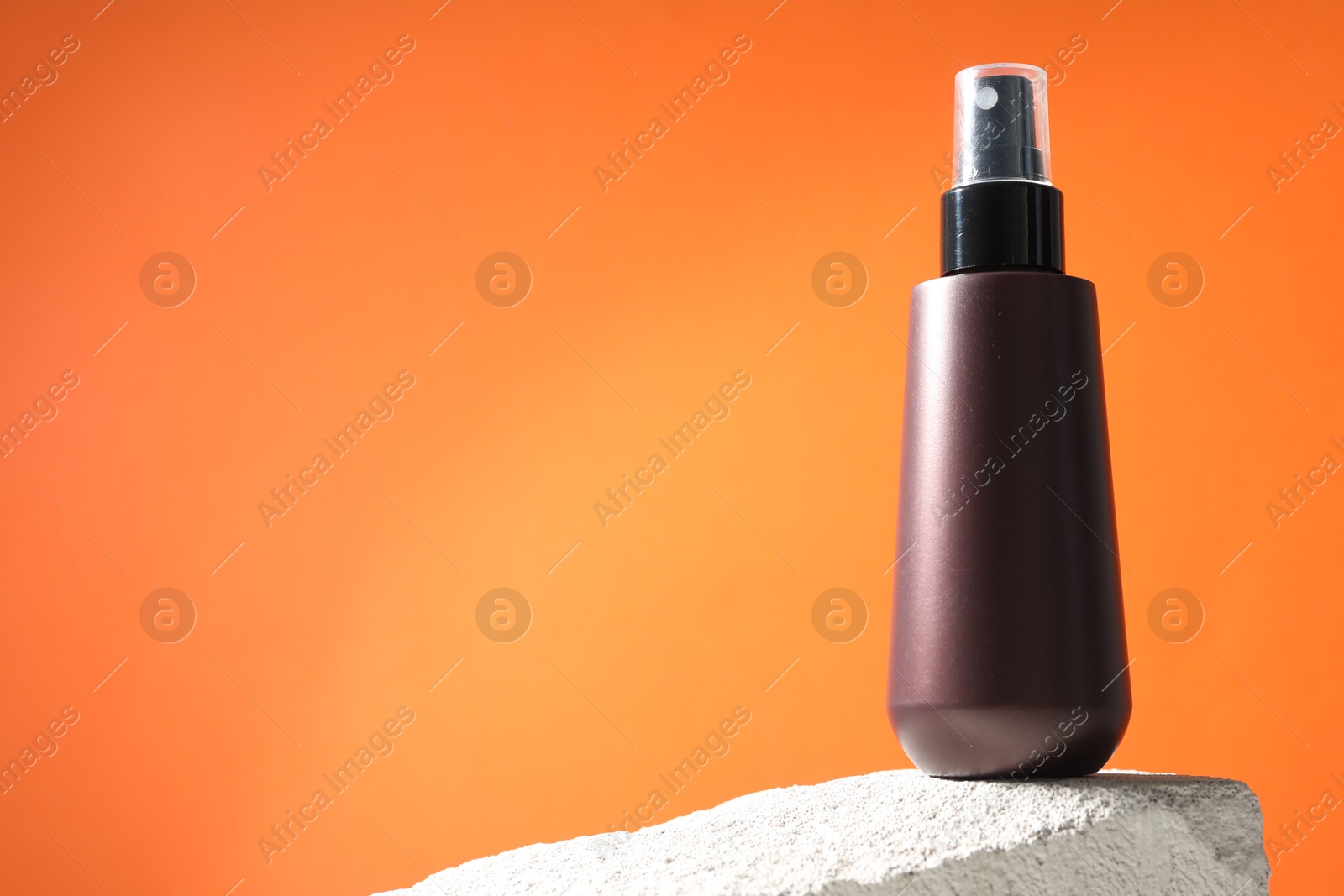 Photo of Bottle of sun protection product on stone against orange background, space for text