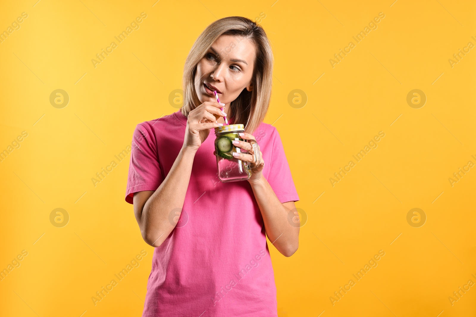 Photo of Woman drinking tasty cucumber water on orange background. Refreshing drink