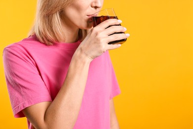 Woman drinking tasty refreshing soda drink on orange background, closeup. Space for text