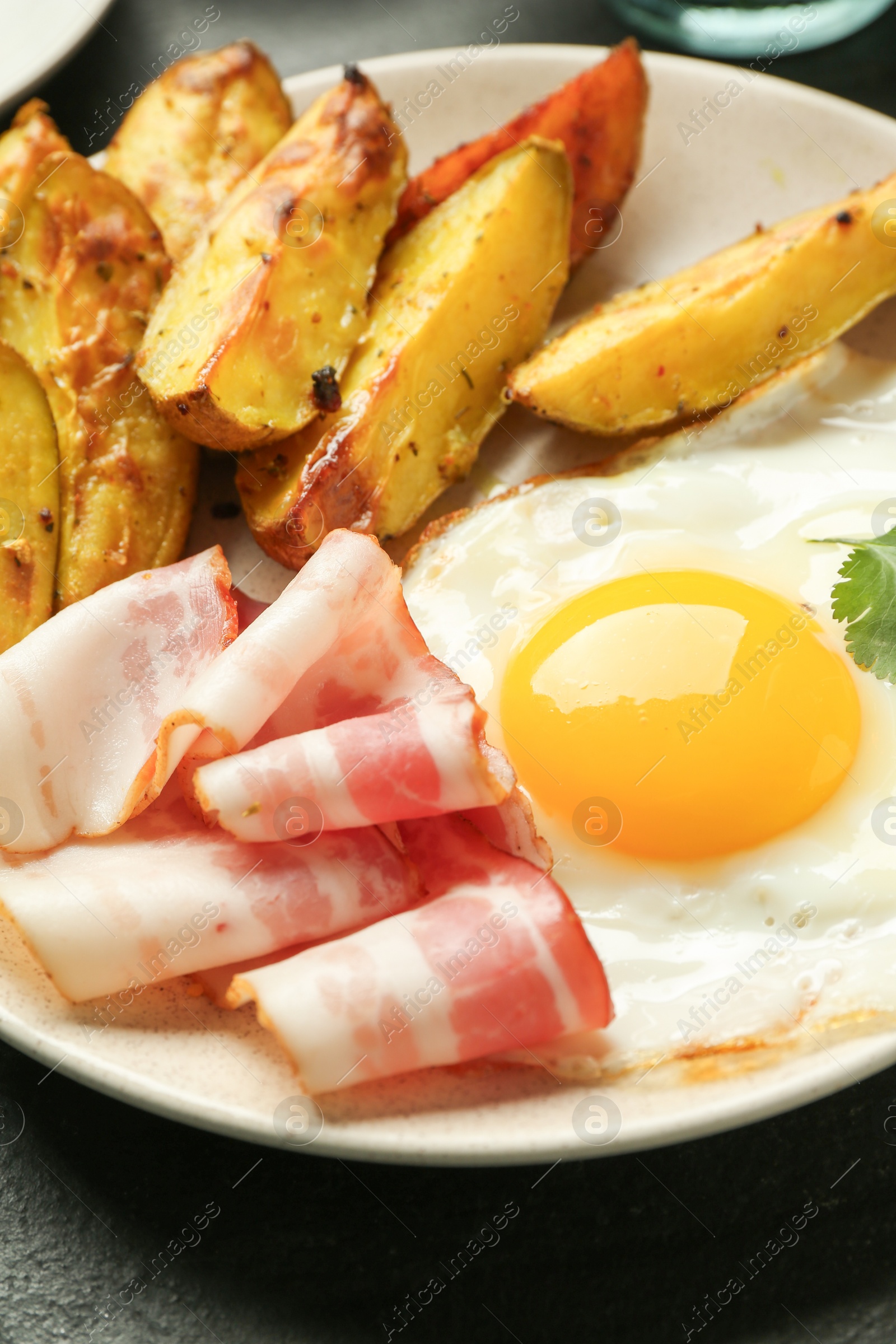 Photo of Tasty brunch. Fried egg, potato and bacon on dark table, closeup