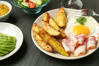 Photo of Tasty brunch. Fried egg, potato, bacon and cut avocado on dark textured table, closeup