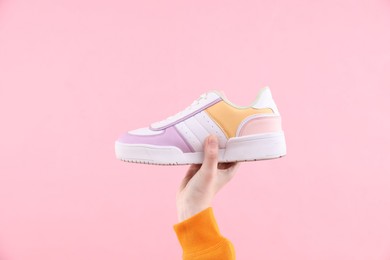 Woman with stylish sneaker on pink background, closeup