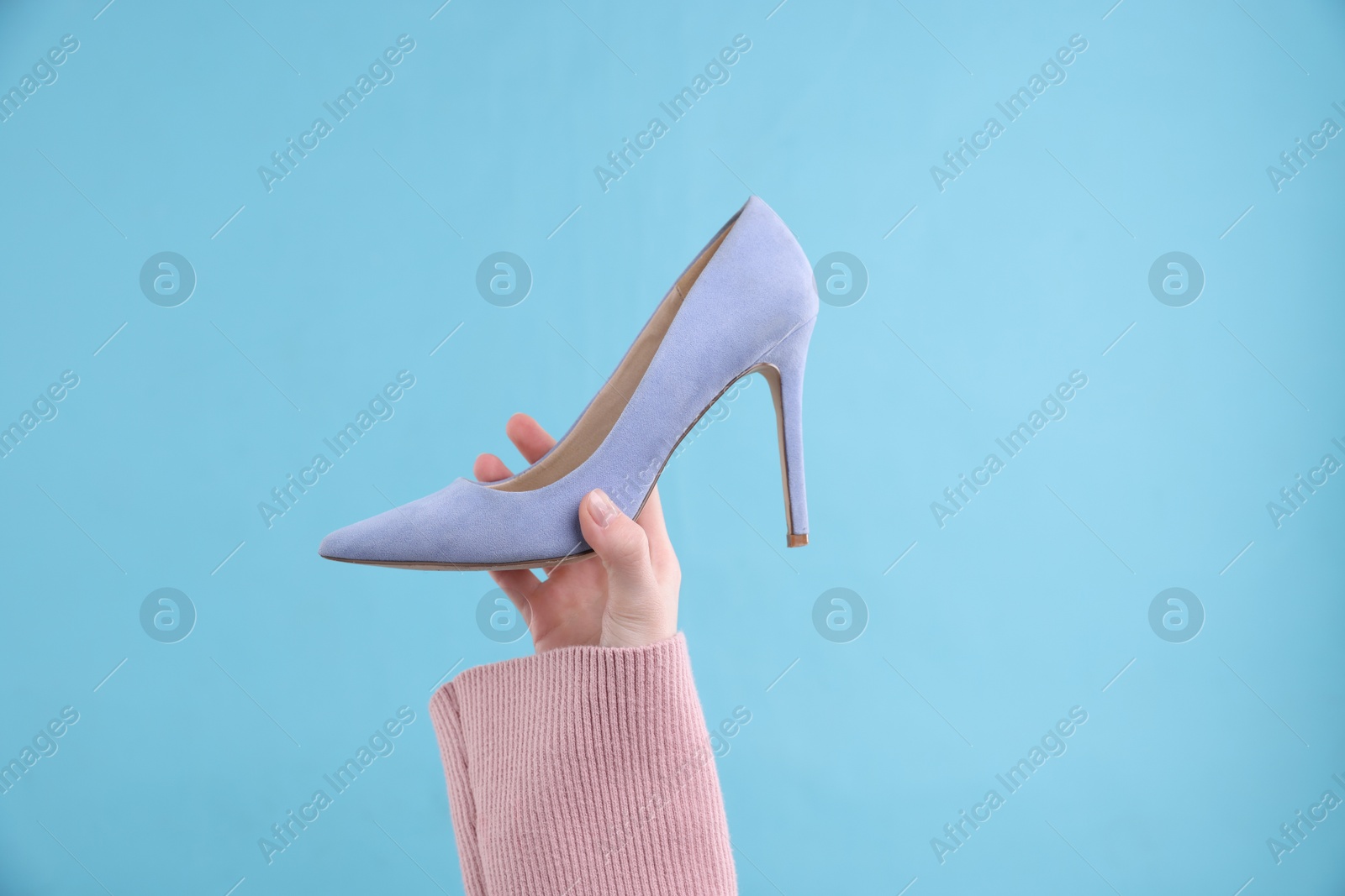 Photo of Woman with high heeled shoe on light blue background, closeup