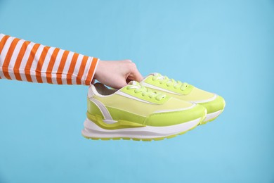 Woman with stylish sneakers on light blue background, closeup