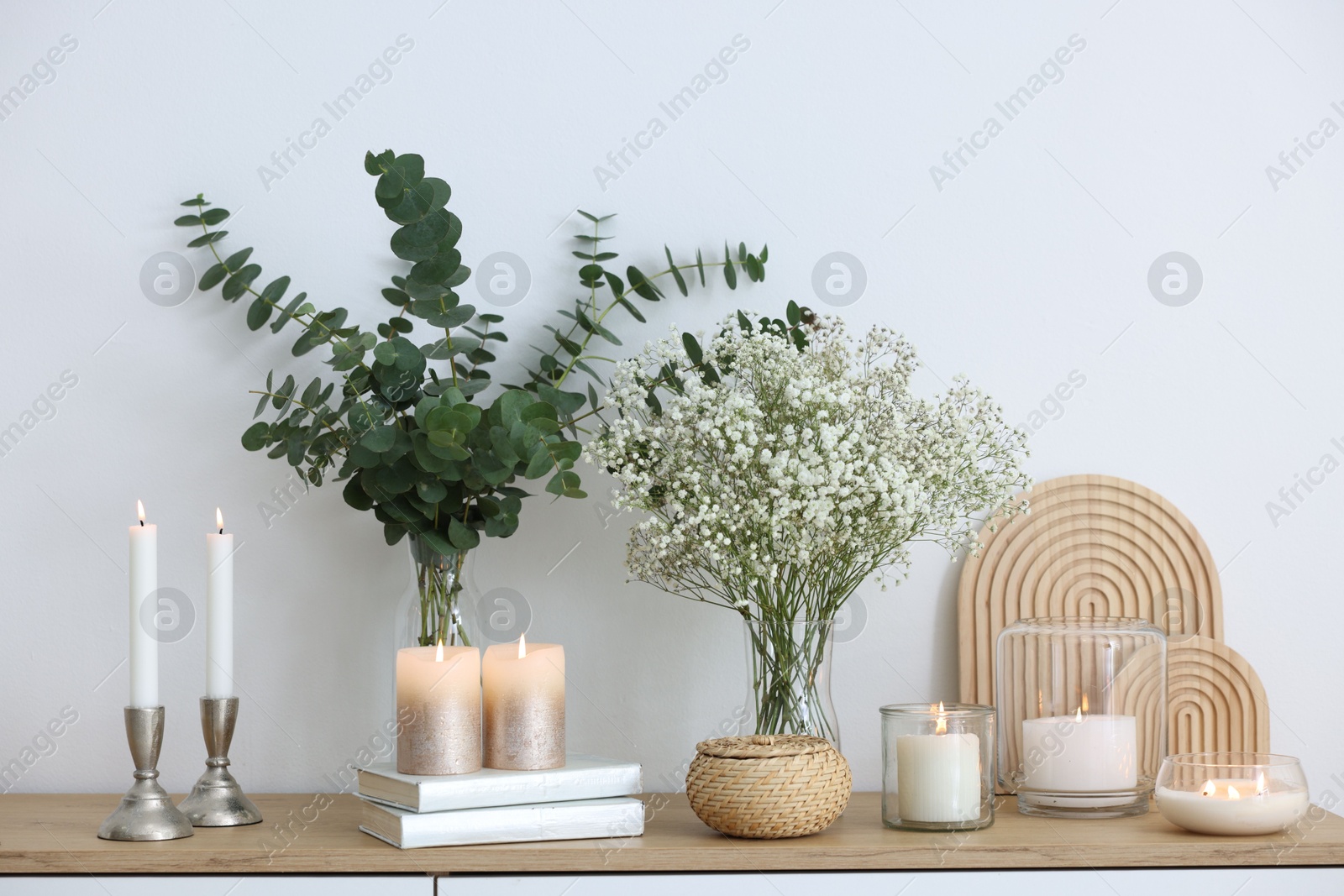 Beautiful gypsophila flowers, eucalyptus branches, burning candles and books on commode at home Photo of Beautiful gypsophila flowers, eucalyptus branches, burning candles and books on commode at home