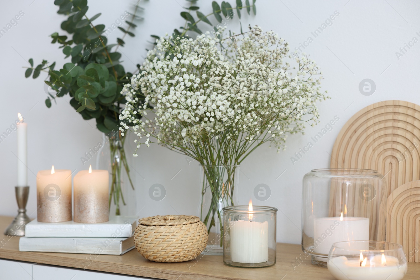 Beautiful gypsophila flowers, eucalyptus branches, burning candles and books on commode at home Photo of Beautiful gypsophila flowers, eucalyptus branches, burning candles and books on commode at home