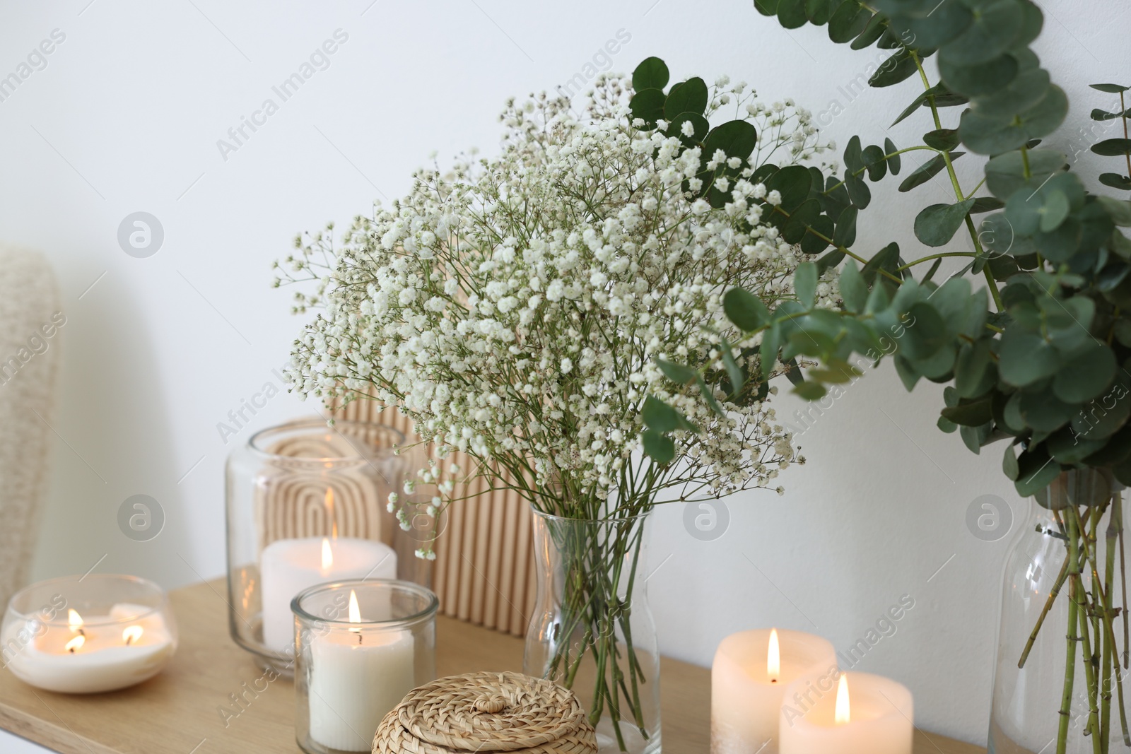 Beautiful gypsophila flowers, eucalyptus branches and burning candles on commode at home Photo of Beautiful gypsophila flowers, eucalyptus branches and burning candles on commode at home