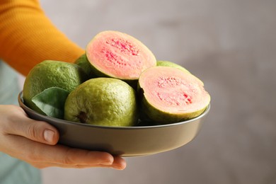 Photo of Woman with bowl of fresh guava fruits on blurred grey background, closeup. Space for text