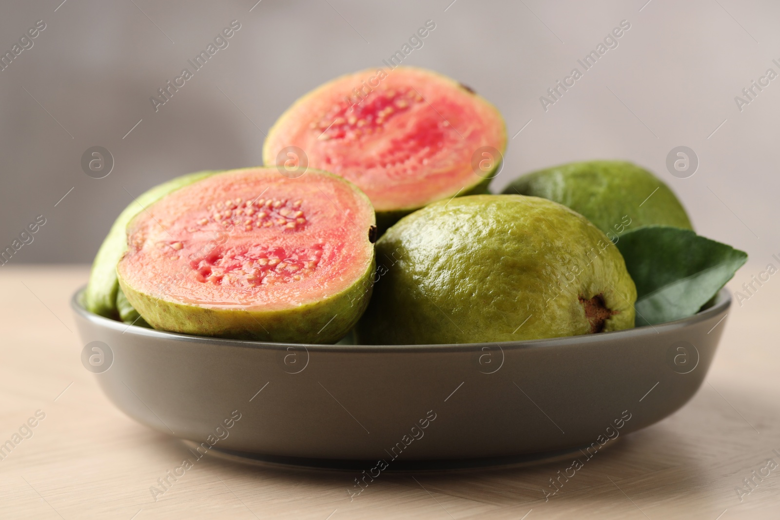 Photo of Fresh guava fruits in bowl on wooden table against blurred grey background, closeup