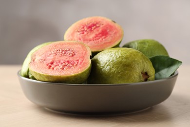 Photo of Fresh guava fruits in bowl on wooden table against blurred grey background, closeup