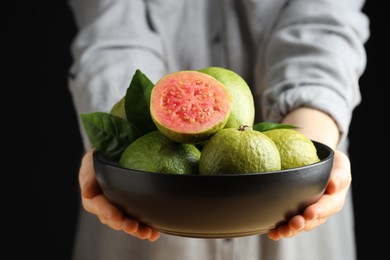 Photo of Woman with bowl of fresh guava fruits on black background, closeup