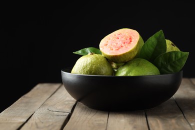 Fresh guava fruits in bowl on wooden table against black background, closeup