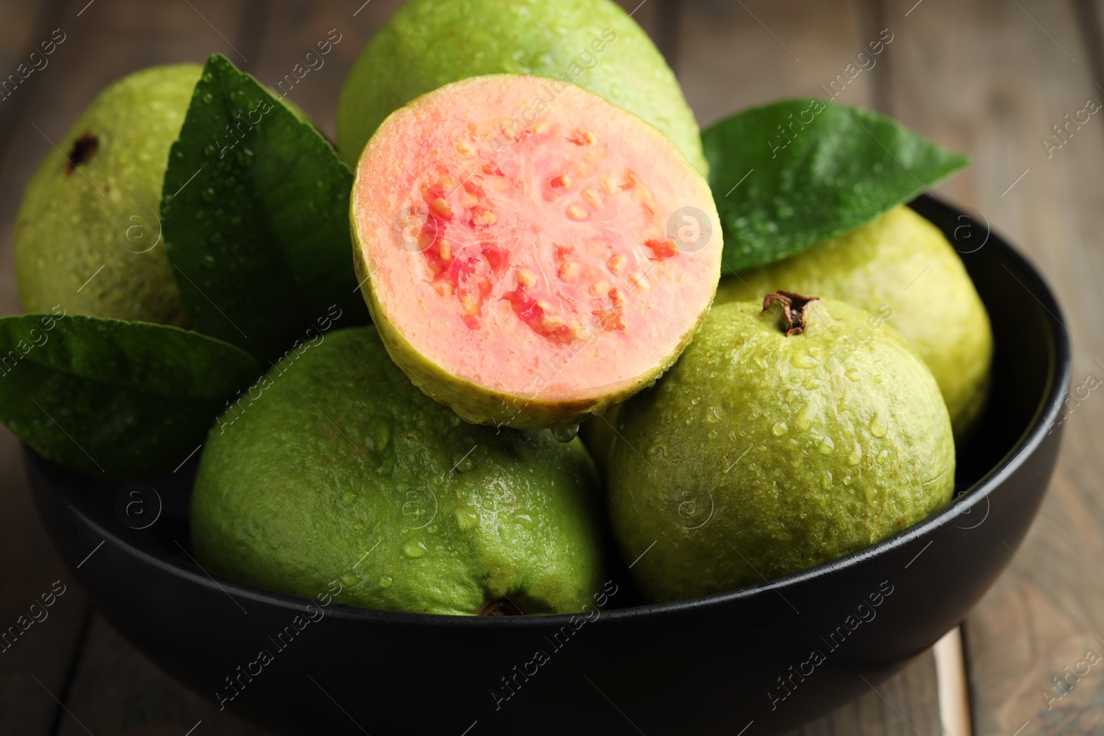 Photo of Fresh guava fruits with water drops in bowl on wooden table, closeup