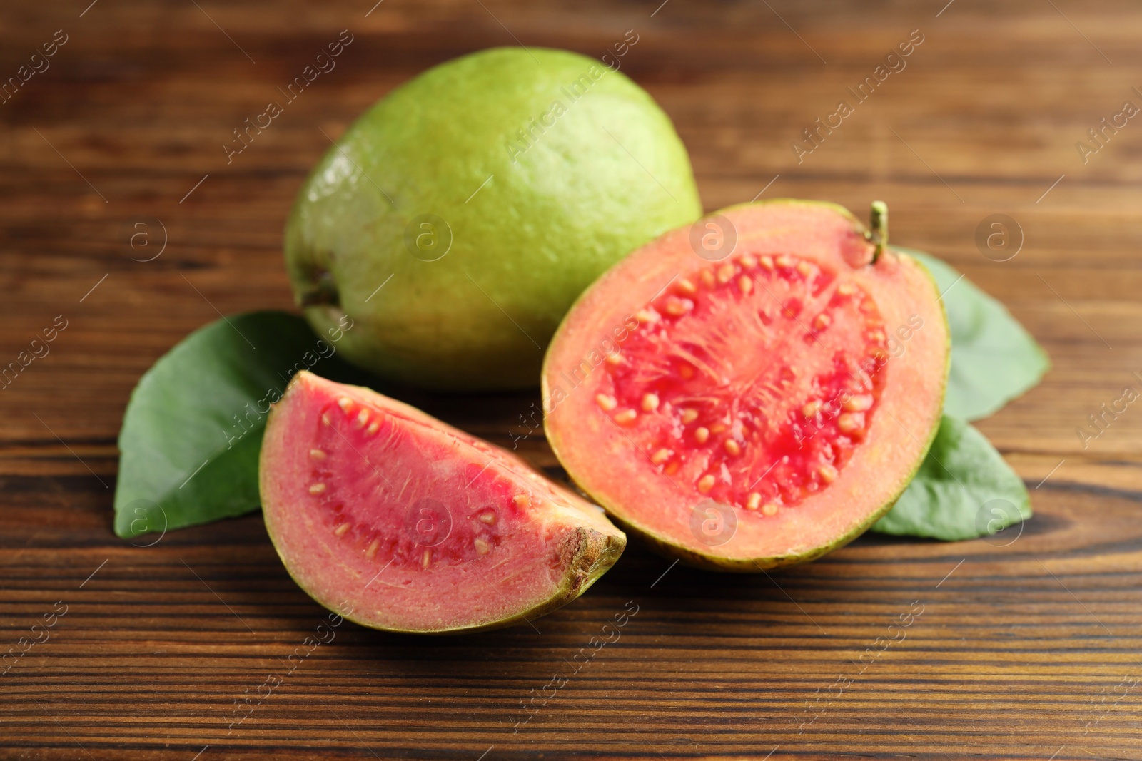 Photo of Fresh cut and whole guava fruits with leaves on wooden table, closeup