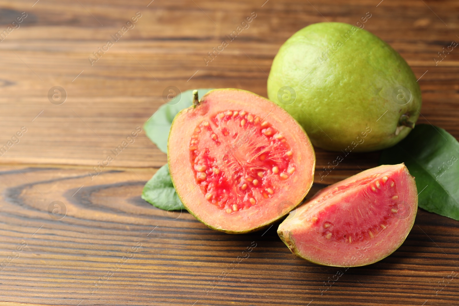 Photo of Fresh cut and whole guava fruits with leaves on wooden table, closeup. Space for text