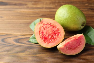 Photo of Fresh cut and whole guava fruits with leaves on wooden table, closeup. Space for text