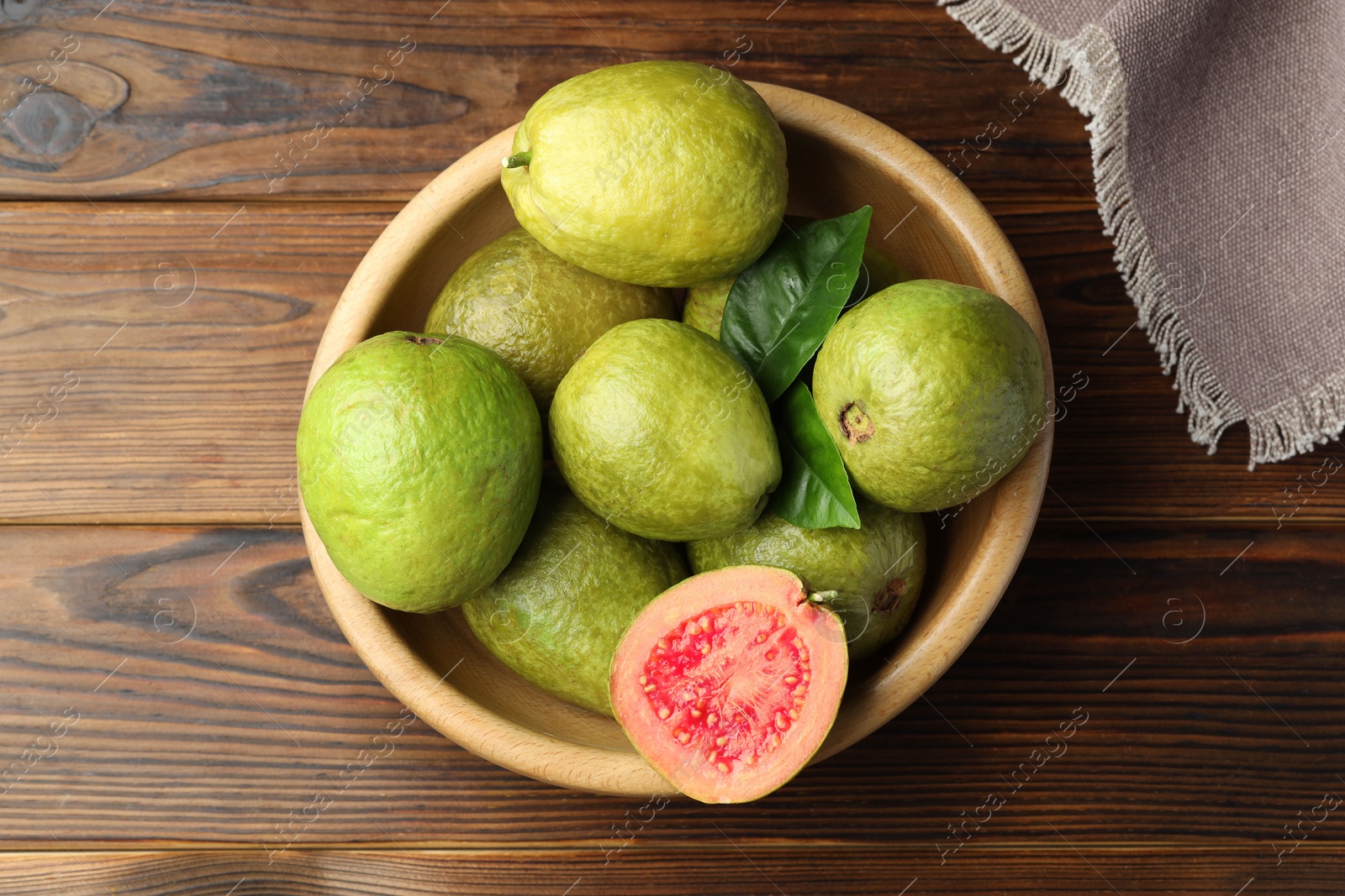 Photo of Fresh cut and whole guava fruits in bowl on wooden table, top view