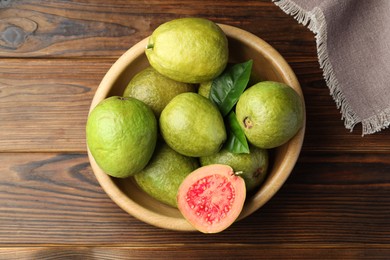 Fresh cut and whole guava fruits in bowl on wooden table, top view